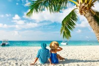 Zamilovaná dvojice sedící na bílé pláže u kokosové palmy, Raa atol, Maledivy