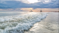 Vlny bijící o písečné pobřeží při západu slunce ve Fort Myers