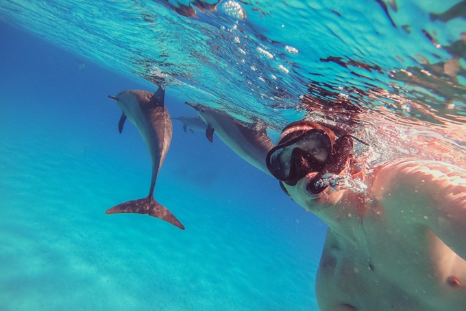 Muž se šnorchlem, který plave s delfíny