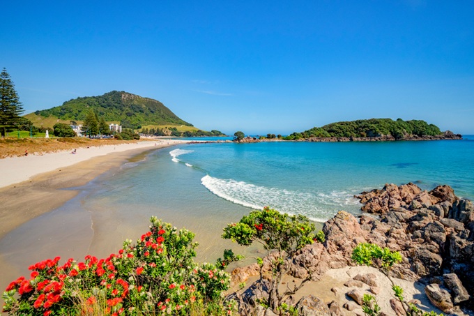 Pláž s tyrkysovým mořem a kopcem v pozadí na Novém Zélandu